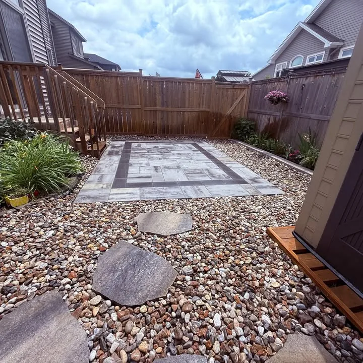 Small paver patio with stepping stones and river-rock border in a fenced yard